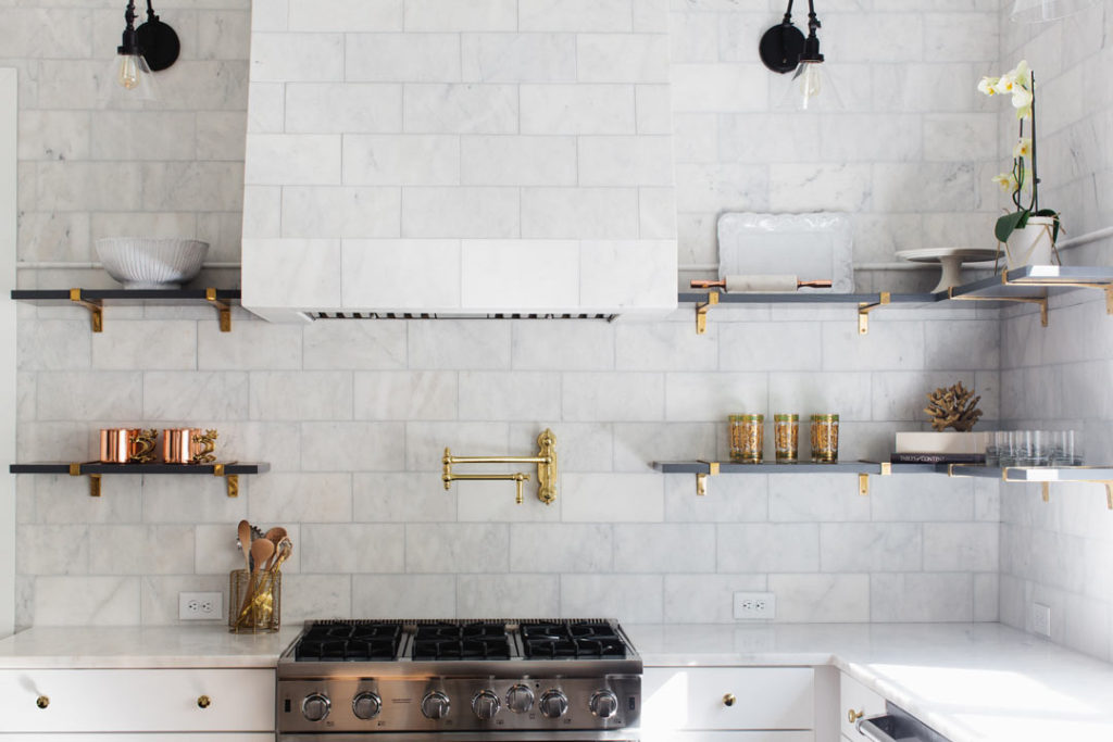 A brass Waterstone pot filler with Alba Vera marble tile for the counter to ceiling backsplash and custom hood.